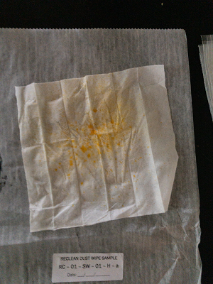 A colorimetric wipe with orange coloration on its surface sits on a plastic mat on a table.