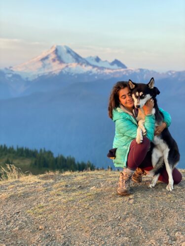 Woman hugging a husky with mountains in background.