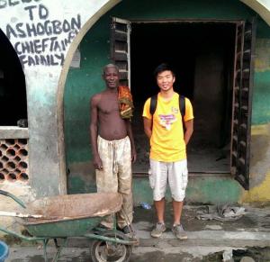 A young man poses with an older man in front of a house in Nigeria.