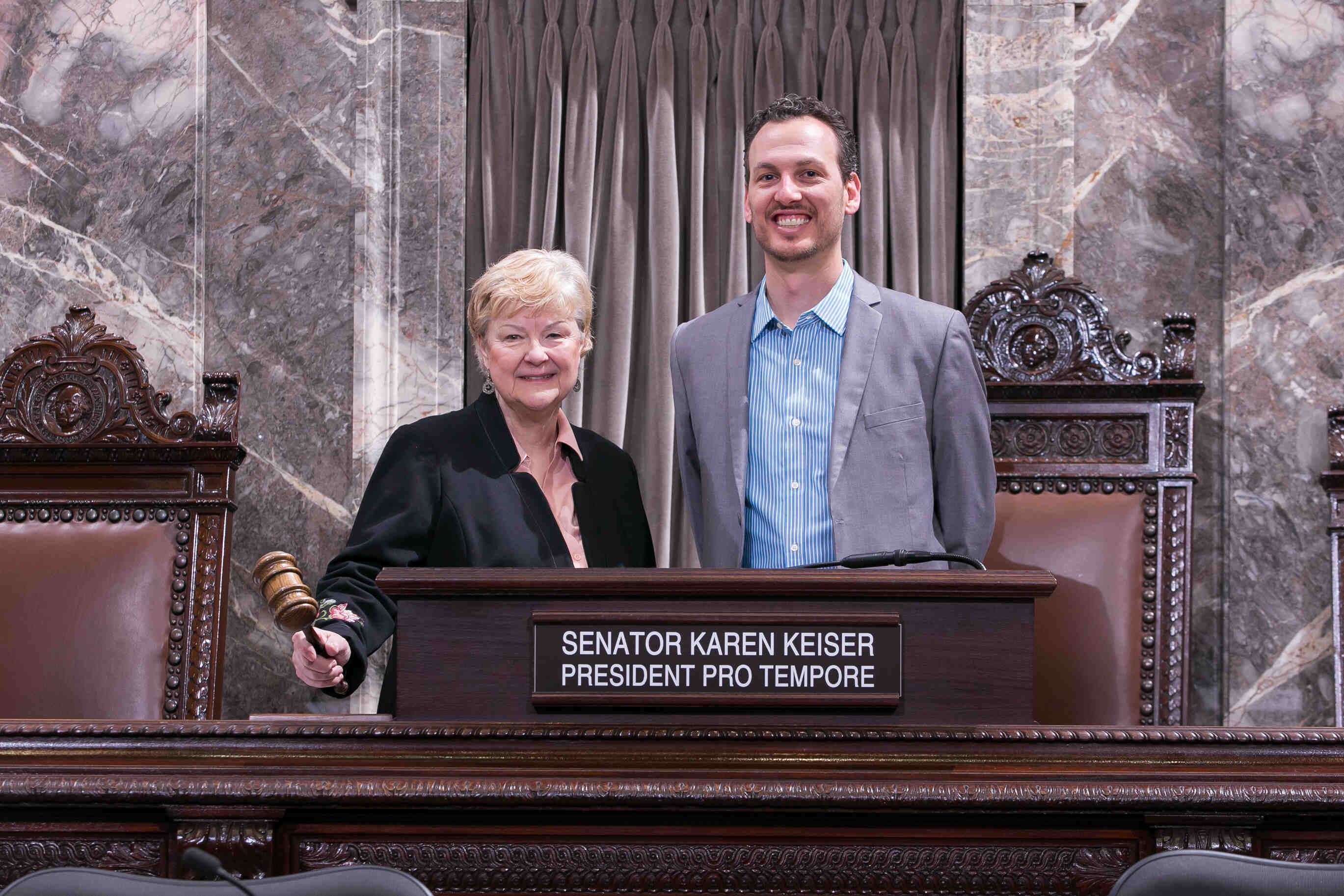 Two people standing at a podium, one holding a gavel.