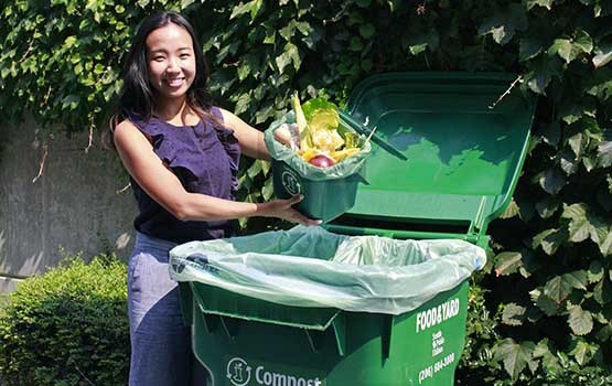 Woman holding food over a compost bin.