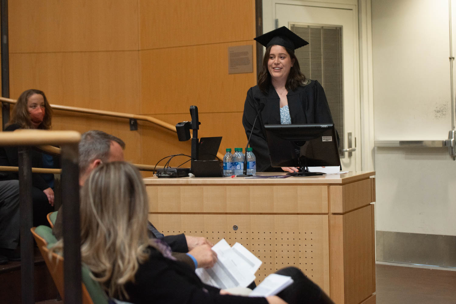 A student in cap and gown speaks at a podium.