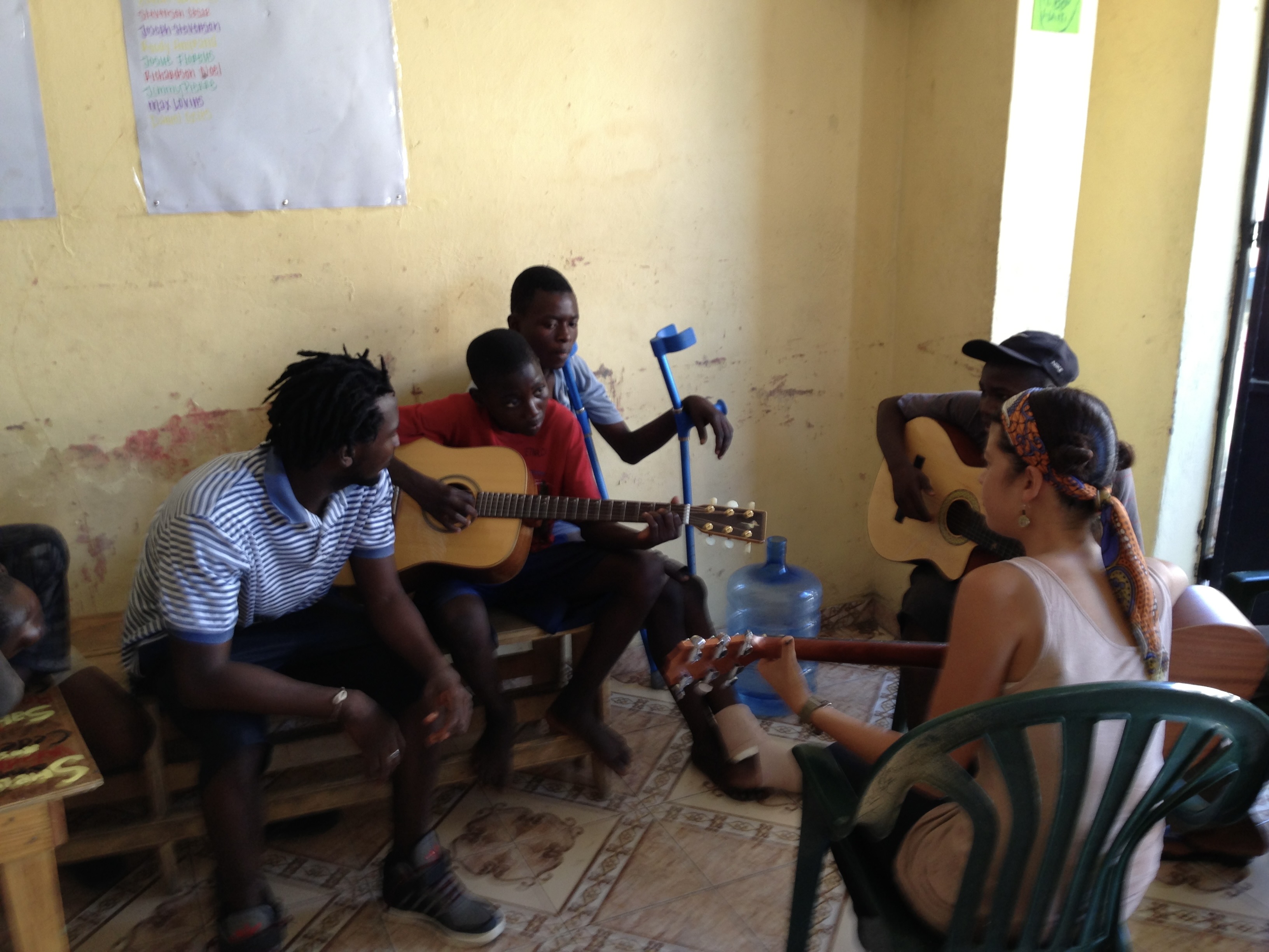 Five people sit around together playing music. Three of them are playing guitars, including Sklar.