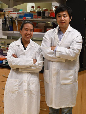 Megumi Matsushita and a fellow scientist stand together in a lab smiling, both in lab coats.