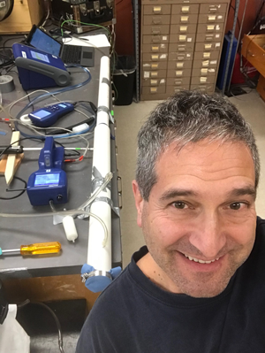 DEOHS Professor Martin Cohen stands in front of a testing setup made with PVC pipe and particle counters for face mask fabrics.
