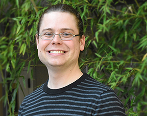 Headshot of Graeme Carvlin standing in front of a green, leafy bush.  Photo by Sarah Fish.