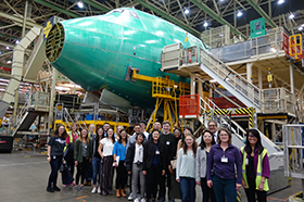 Group of DEOHS students stand in front of an airplane that is being built in a large warehouse space.