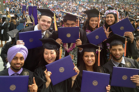 A group of students in graduation garb hold up their diploma folders.