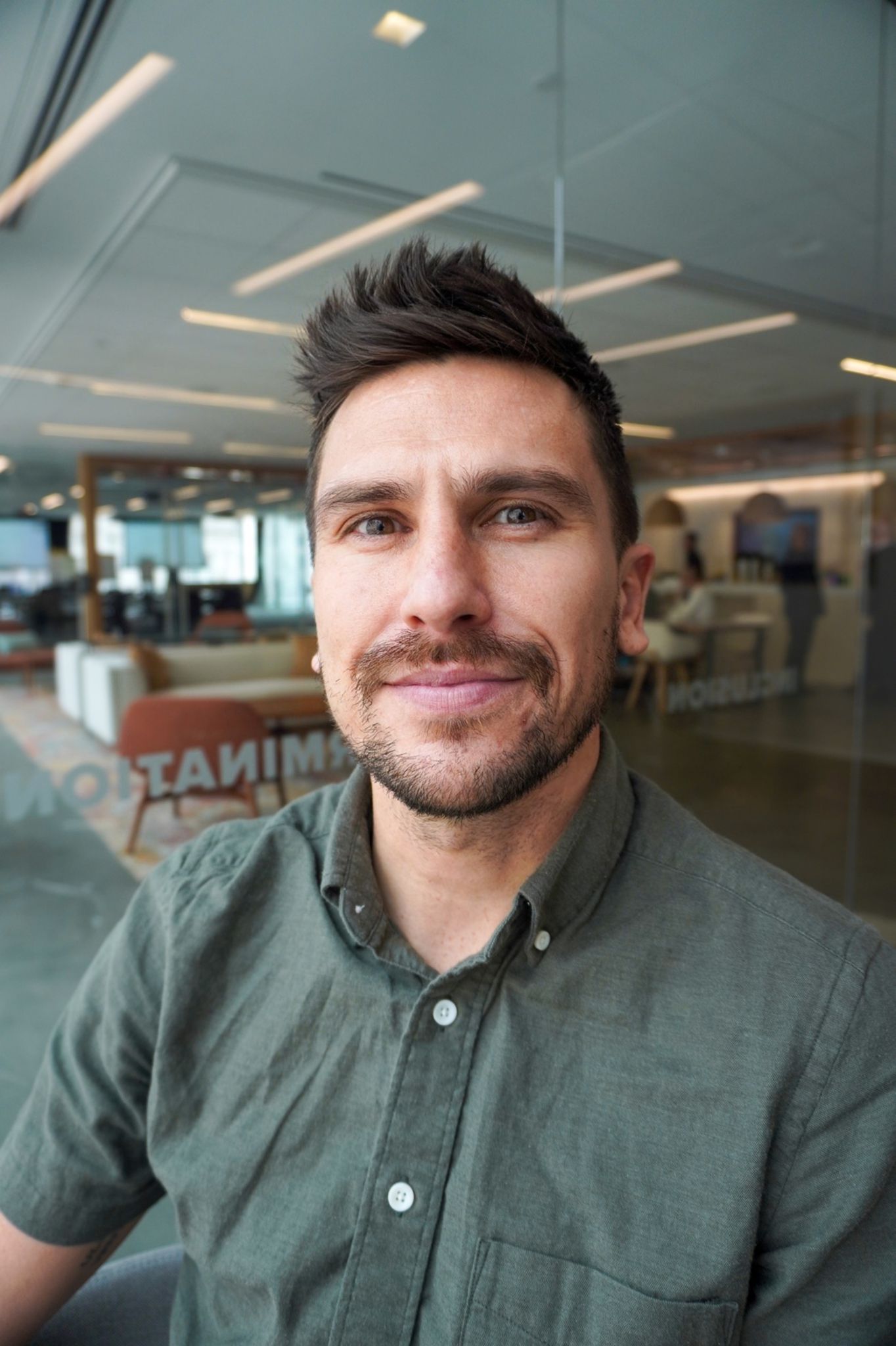 A smiling man with short brown hair and a green shirt. 