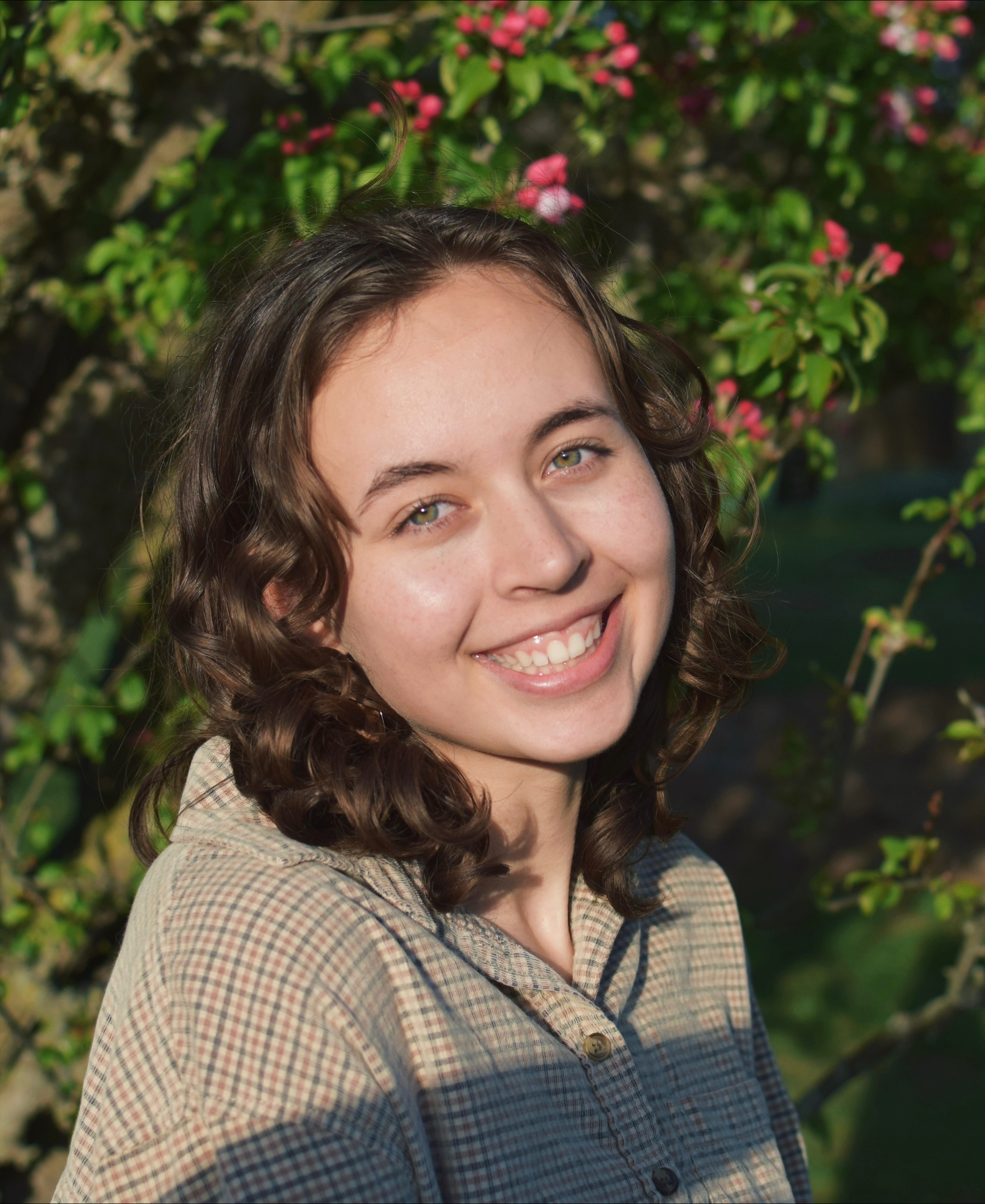 A smiling woman with curly brown hair wearing a tan shirt.