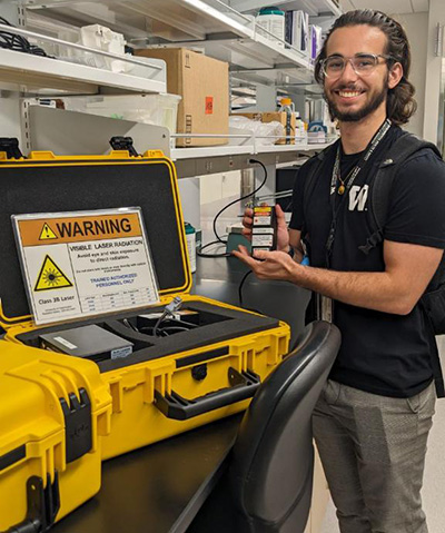 A man with glasses poses next to a yellow case with a Warning label on it.
