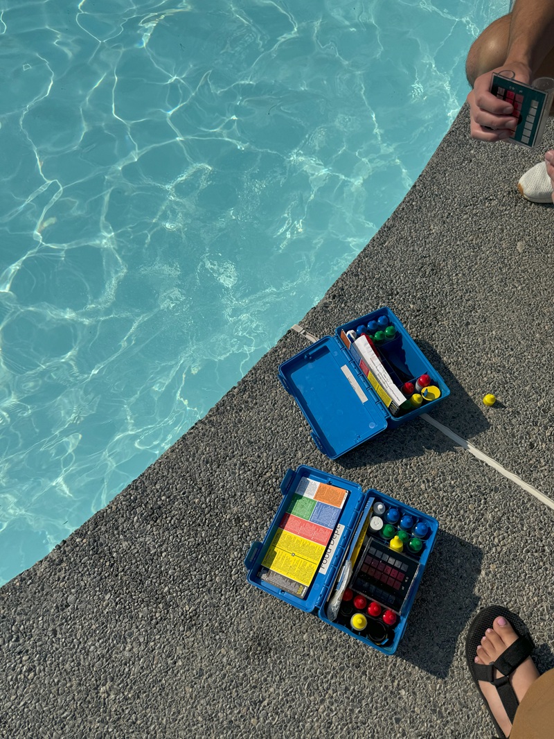 Image of pool water and concrete edge with feet visible and pool chemicals in a blue plastic box