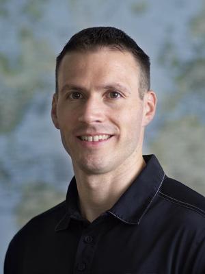 Photo of Cory Morin, a young white man with short brown hair wearing a black polo shirt