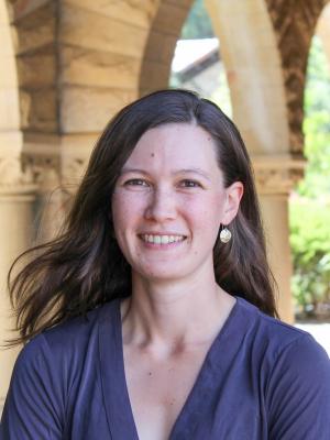 Smiling woman with long brown hair in a purple shirt with arches in background