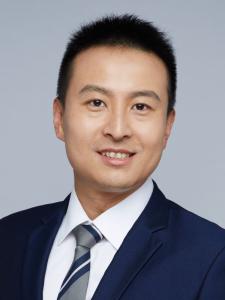 Man with short black hair in dark blue suit, gray and blue tie