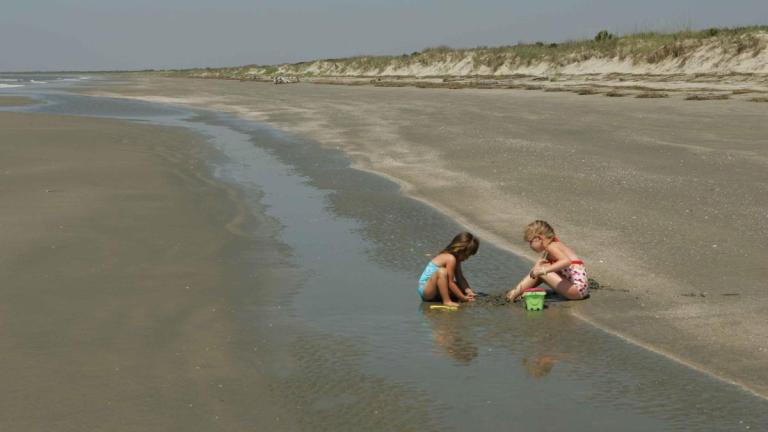 Two children play in the sand on a beach at the water's edge.