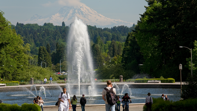 A group of students walk and bike around a fountain with a view of a snow-covered mountain in the distance.