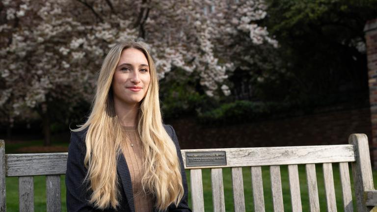 Abbie Gilbert sits on a bench on the UW campus with cherry blossoms in the background.