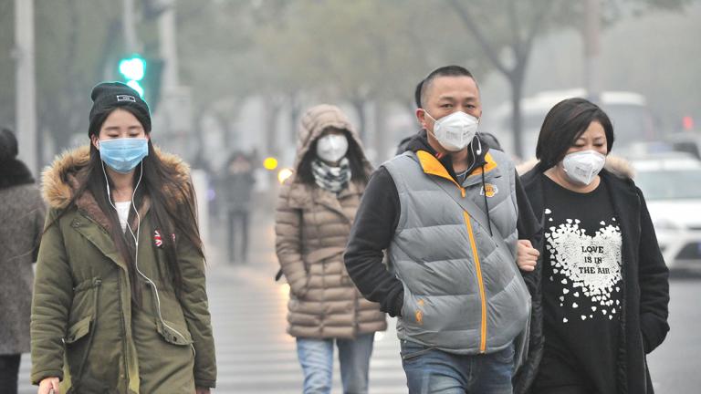 A group of Chinese pedestrians wear face masks while walking in smog.
