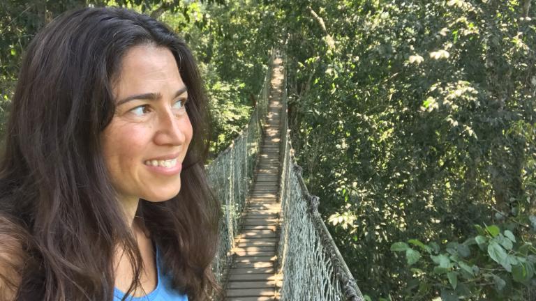 Woman looking to the right with a rope and wood bridge behind her in a forested landscape.