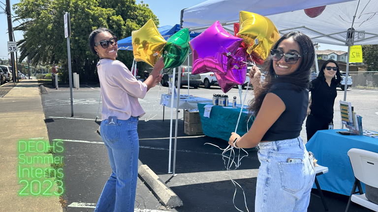 two women holding balloons decorate an outdoor booth