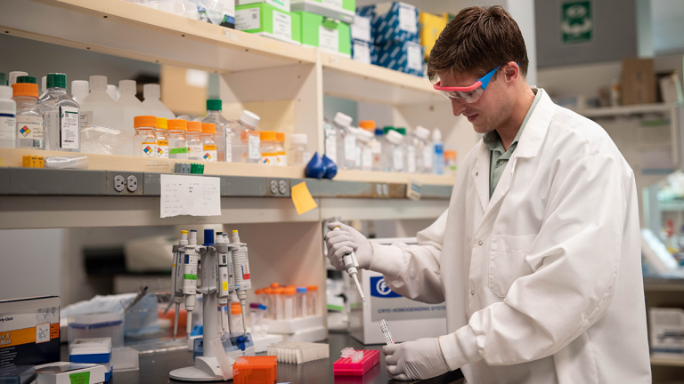 Student in a white lab coat working in a lab. 