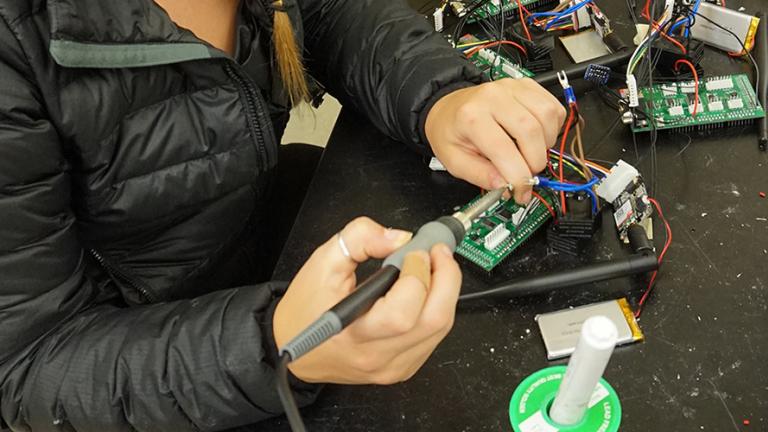 Close up of UW student Natalia Kowalchuk's hands holding a soldering iron as she builds an air monitor in a lab. Photo: Kayla Cayton.