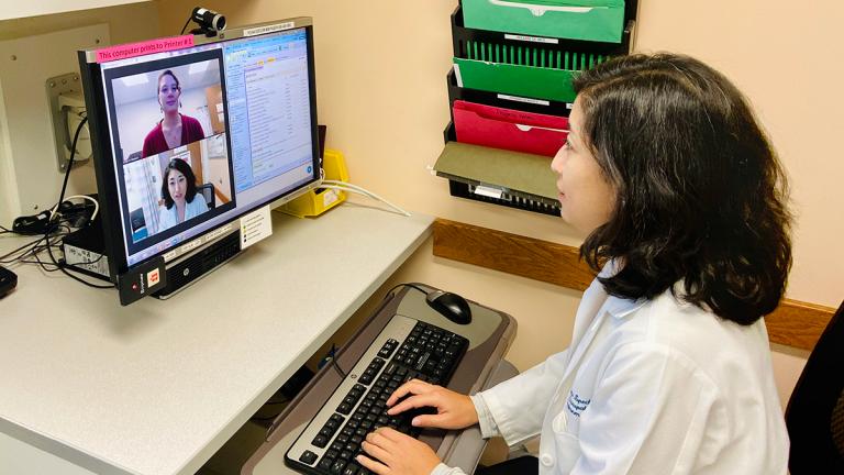 A doctor sits in front of a computer with a video image of herself and a patient.