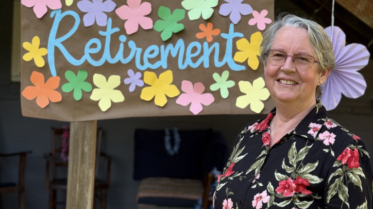 Lianne Sheppard smiles in front of a poster reading "Retirement" with flowers on it.