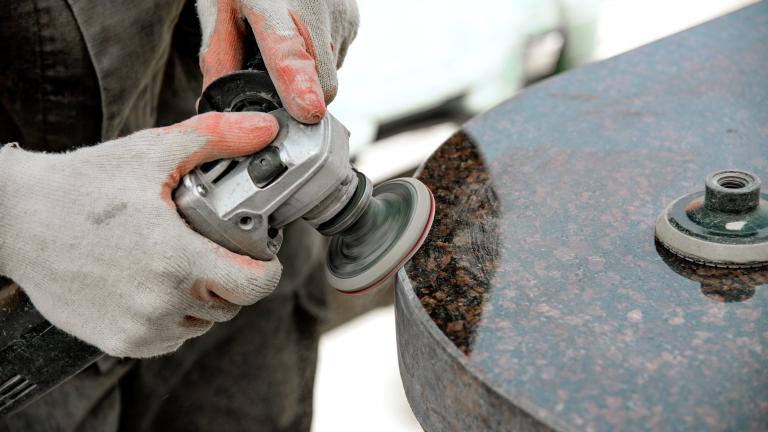 A worker's hands polish a countertop with a power tool.