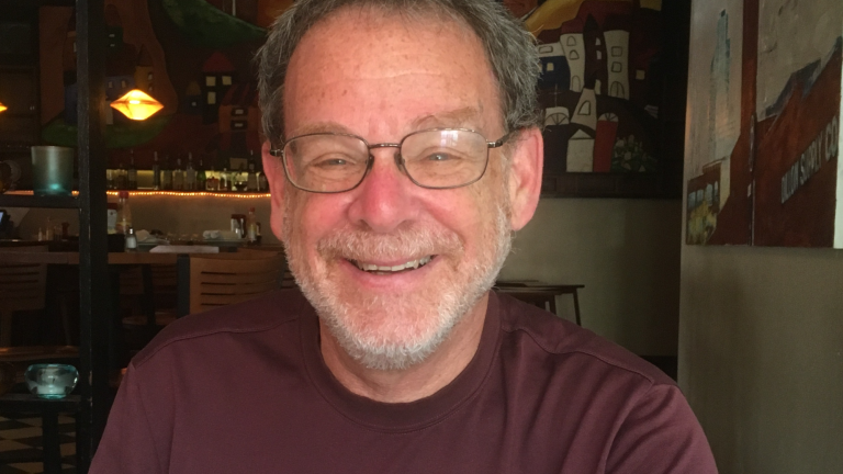 Robert Harrison wears long sleeved shirt and glasses while smiling at the camera