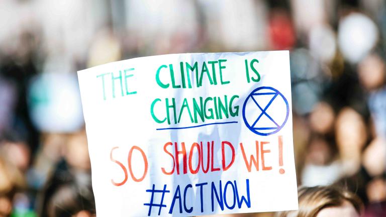 A white sign held up during a rally says, "The climate is changing. So should we. Act now!"