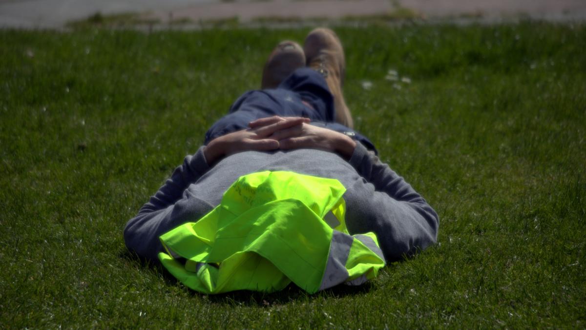 A construction worker rests on grass with a safety vest over his face.