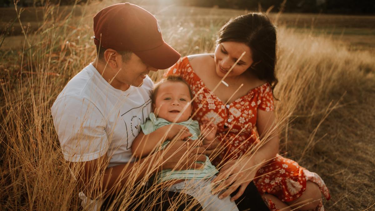 A man and woman hold a smiling child in a field of tall grasses.