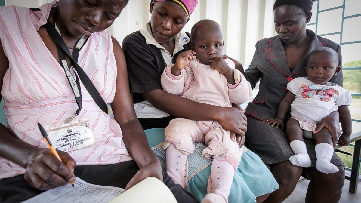 Two Kenyan mothers sit with their babies next to a health care worker.