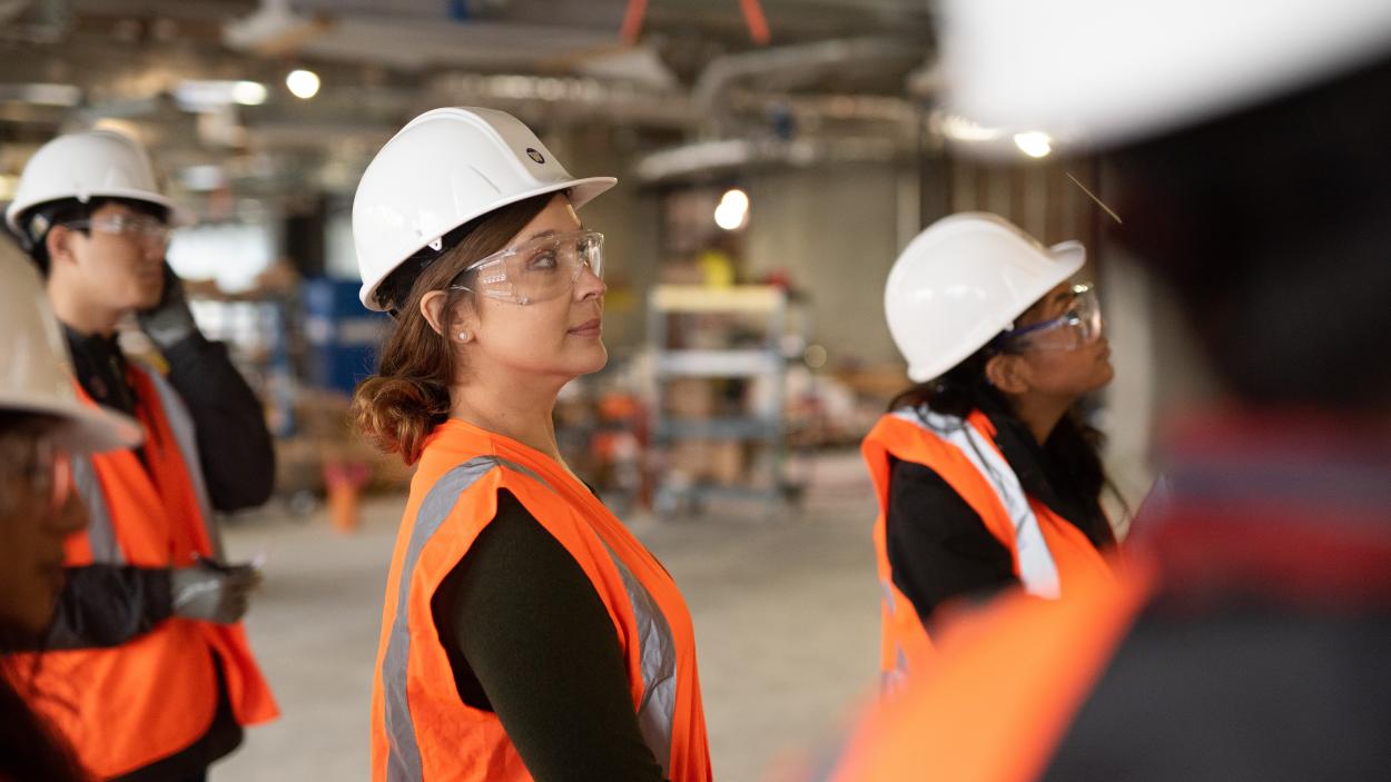 Dennise Drury stands in a hard hat and safety vest in an industrial space with other students around her.