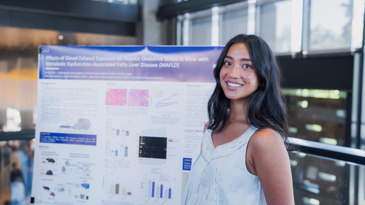 Emily Do smiles in front of her research poster.