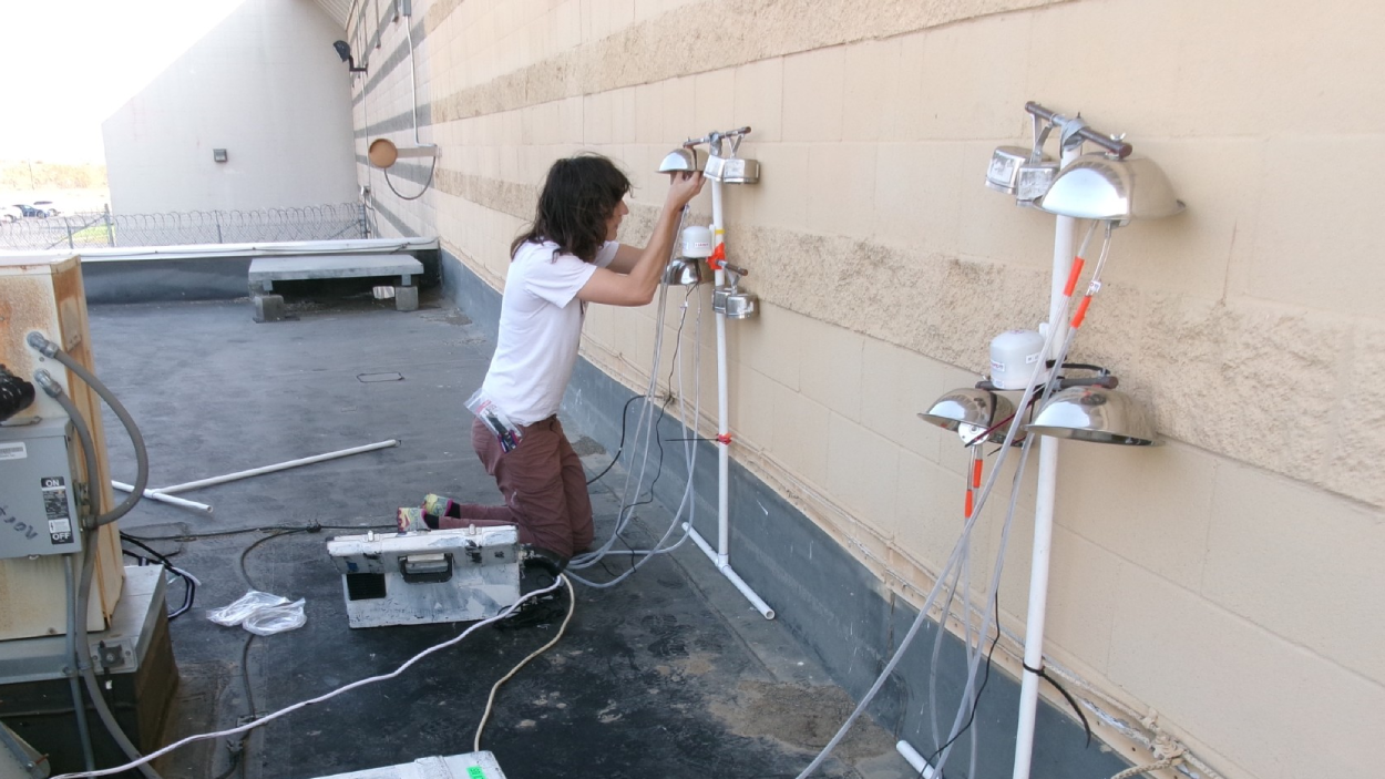 Beck Kiely works with air monitoring equipment on the outside wall of a correctional facility.