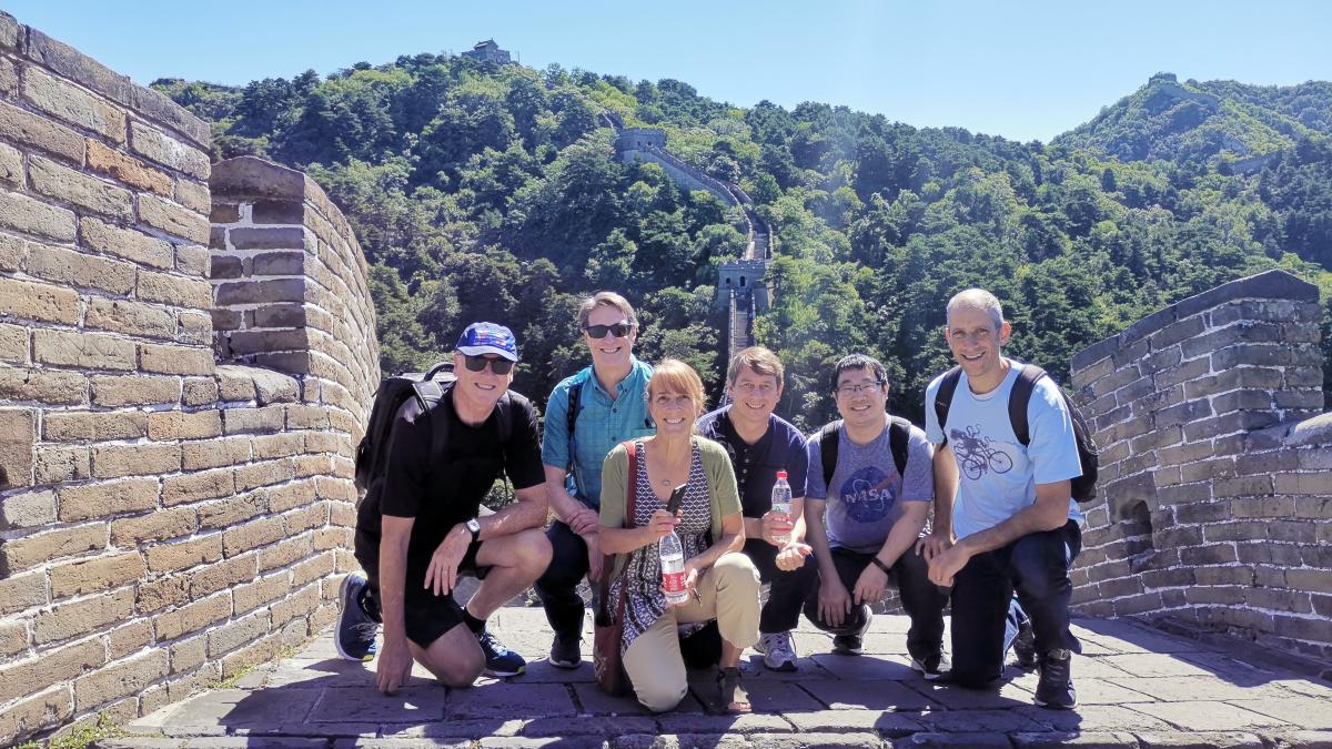 Six people smiling and kneeling on a brick walkway that is part of the Great Wall of China.