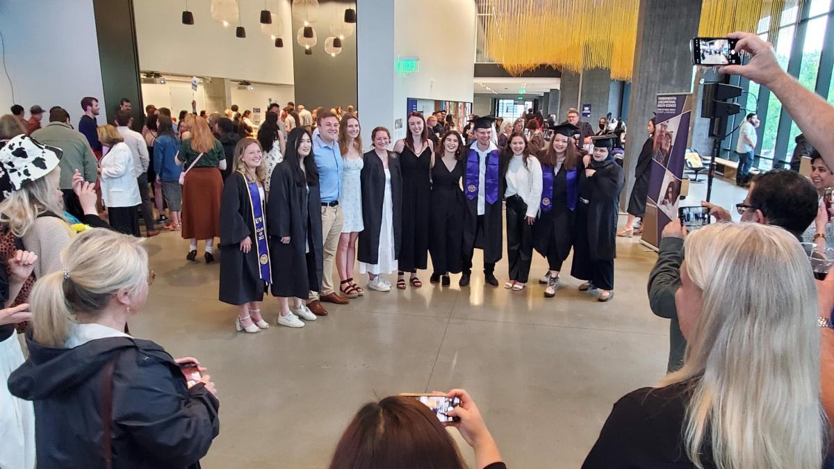 A group of UW students, some wearing graduation robes, pose for their families to take photos. 