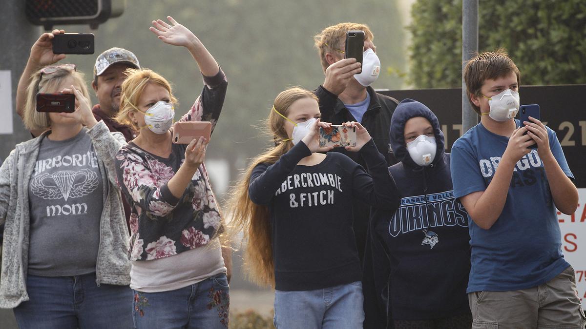 A group of people stand on a street wearing air masks and taking video on their cellphones.