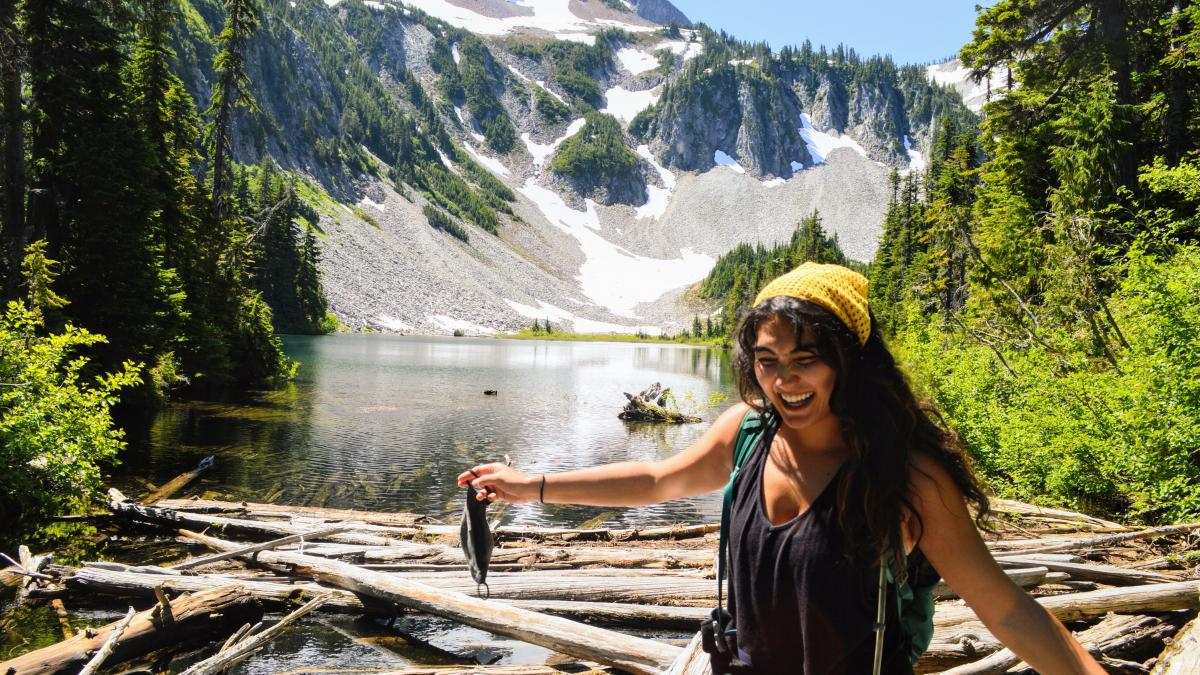 Alexandria Vingino standing in front of a lake and mountain, with a cloth face mask in hand.