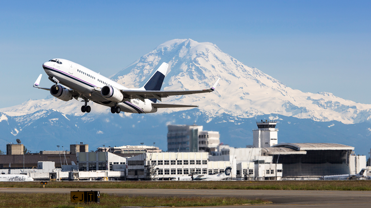 A jet airplane takes off from Sea-Tac Airport, with Mount Rainier in the background.