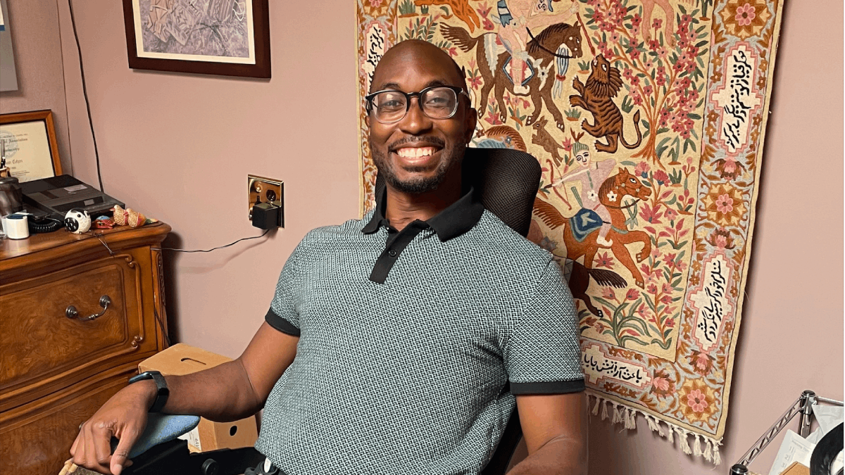 Alawode sits in an office in a clinic with a tapestry behind him. 