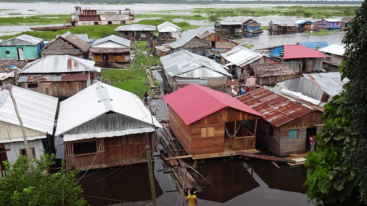 Photo of floating houses in Peru made of wood and corrugated metal propped up on piers with floodwater underneath.