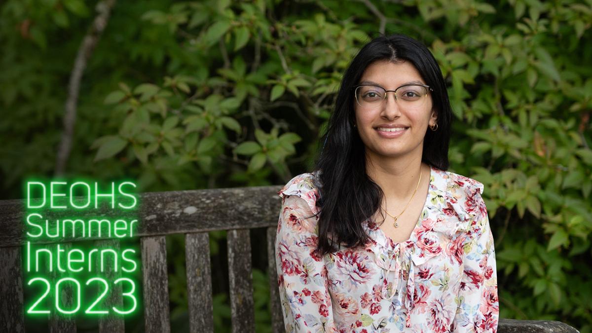 Anika Rajput sits on a bench on the UW campus with greenery in the background.