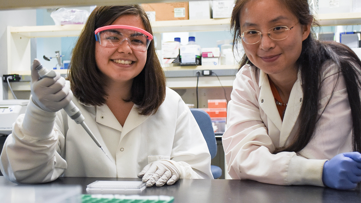 Two women in white lab coats work together in a lab.