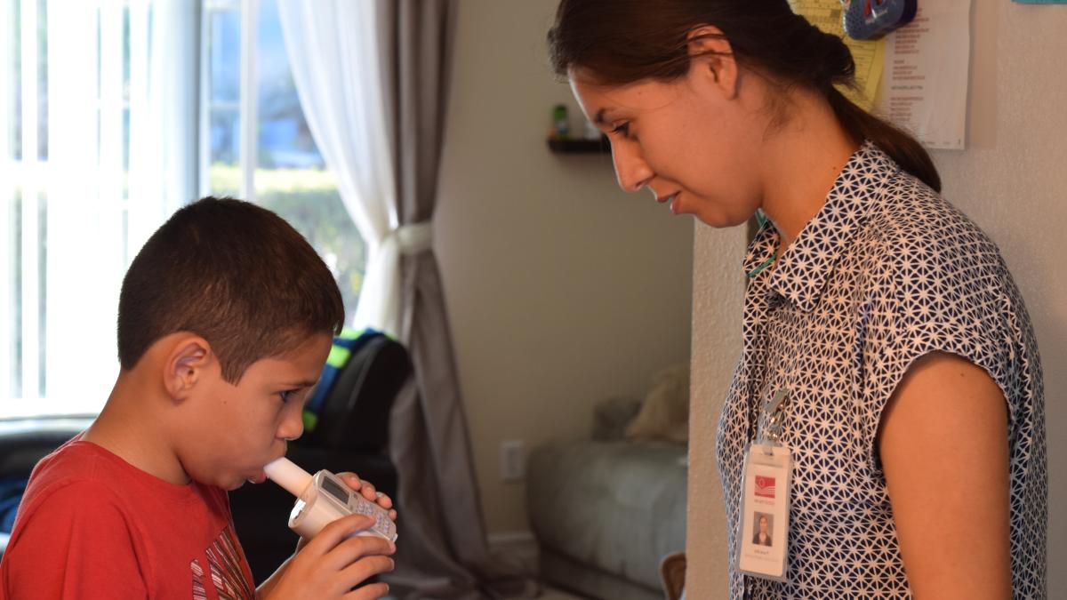 A woman looks on as a boy blows into a respiratory monitoring device.