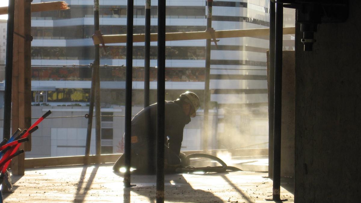 Construction worker sanding a floor with dust flying up