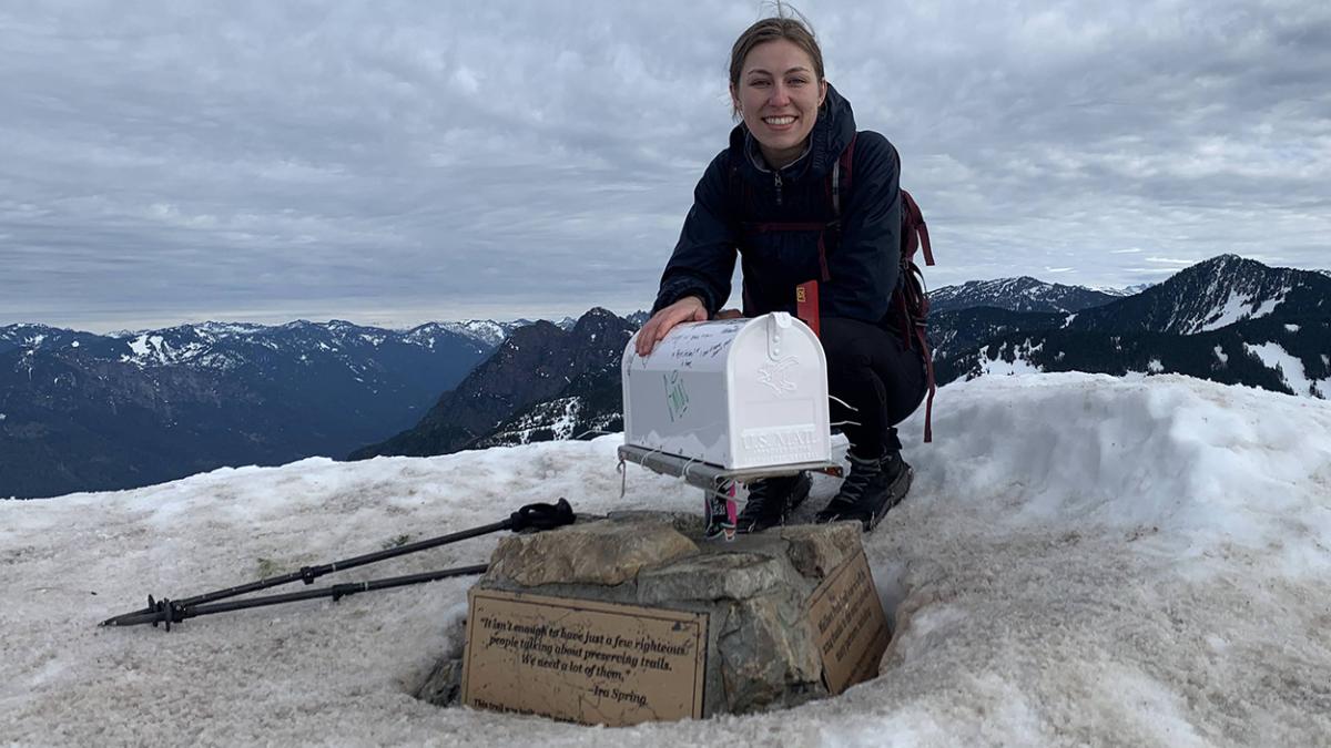 Becky Kann crouches atop snow-covered Mailbox Peak in Washington behind a mailbox.